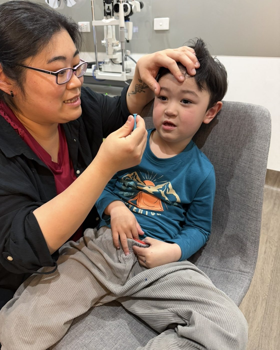 A mother holding her son's eyelid open and bringing an Ortho-K lens to his eye on the insertion plunger