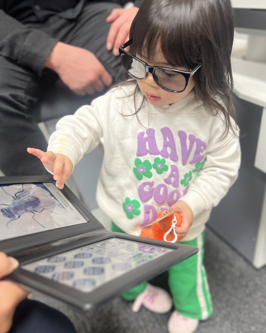 A toddler in glasses pointing at pictures on a tablet during a vision check
